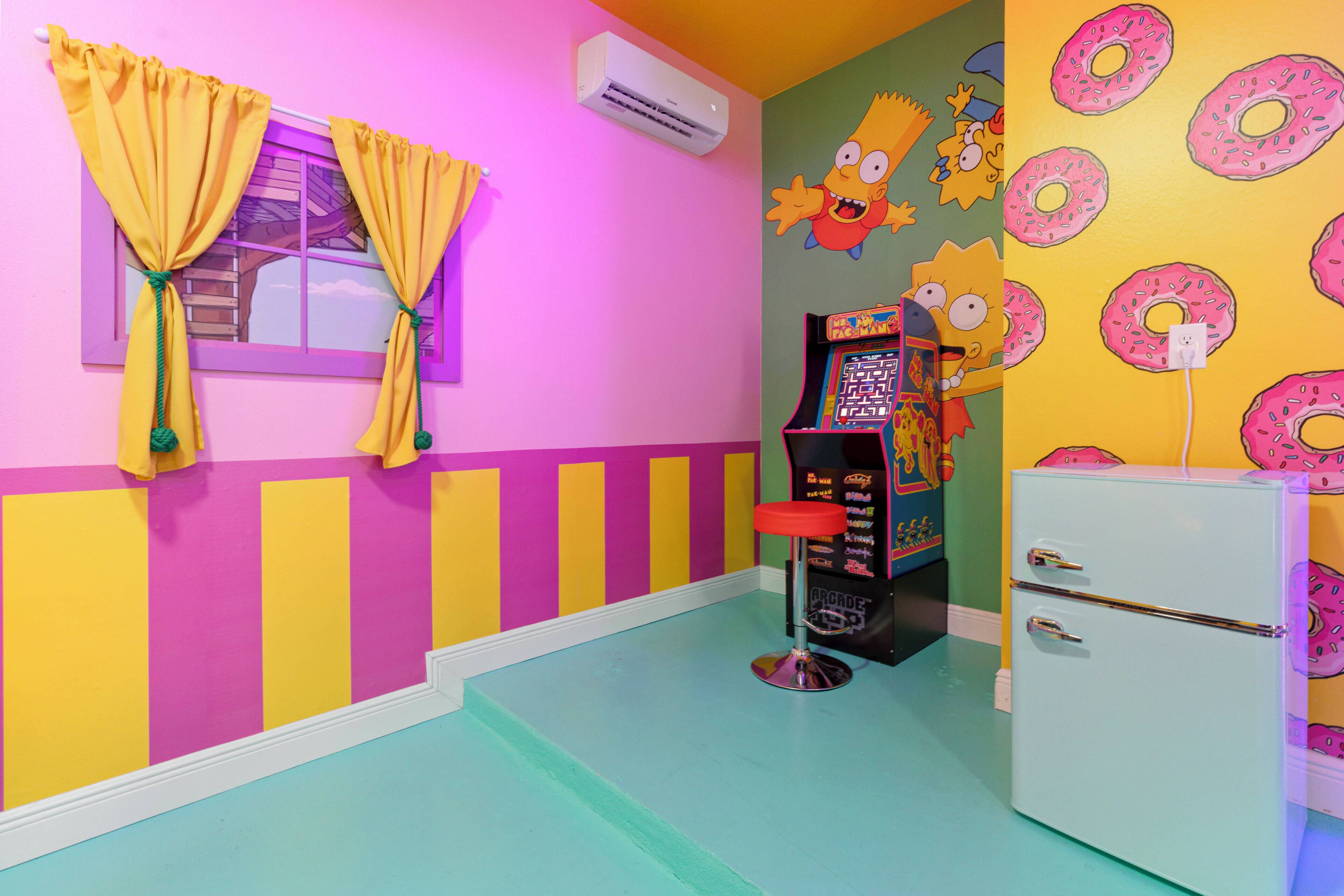 A brightly colored room with a window, air conditioning unit, arcade game, and a refrigerator.