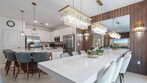 A modern kitchen with a large island, bar stools, pendant lights, and a large mirror.