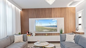 A modern living room with a grey sofa, a coffee table, and a flat-screen TV mounted on a wooden wall.