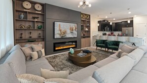 A modern living room with a fireplace, a large sofa, and a dining area with a kitchen in the background. - 9BR house sleeps 22 with private pool in kissimmee (Kissimmee)