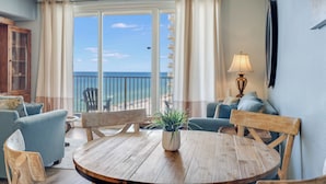 Ein Zimmer mit einem Holztisch, zwei Stühlen, einer Couch, einer Lampe und einem Blick auf den Ozean durch große Fenster.