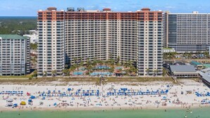 Ein Hochhaus-Hotel mit mehreren Etagen, ein Strand im Vordergrund und ein klarer, blauer Himmel.