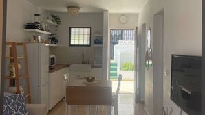 Eine moderne Küche mit weißen Schränken, einer Mikrowelle und einem Mixer auf der Arbeitsfläche. Ein Esstisch mit Stühlen und ein Fernseher auf einem Schrank sind ebenfalls vorhanden.