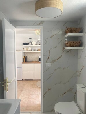 Un baño moderno con paredes de mármol, un inodoro blanco y un lavabo. Hay cestas de mimbre en estantes sobre el inodoro.