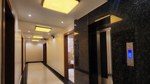 A modern hotel corridor with a shiny floor, recessed lighting, and a digital elevator display. - Kashi Vilaa (Varanasi)