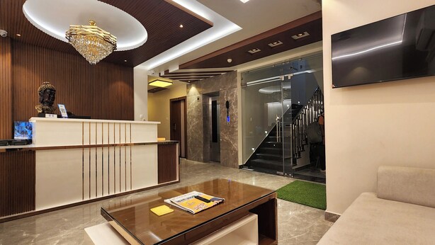 A modern lobby with a reception desk, a coffee table with a magazine, a chandelier, and a staircase leading to an elevator. - Kashi Vilaa (Varanasi)