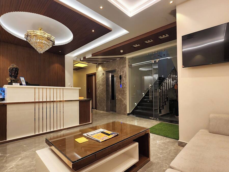 Un vestíbulo moderno con un mostrador de recepción, una mesa de centro con una revista, una araña y una escalera que conduce a un ascensor.