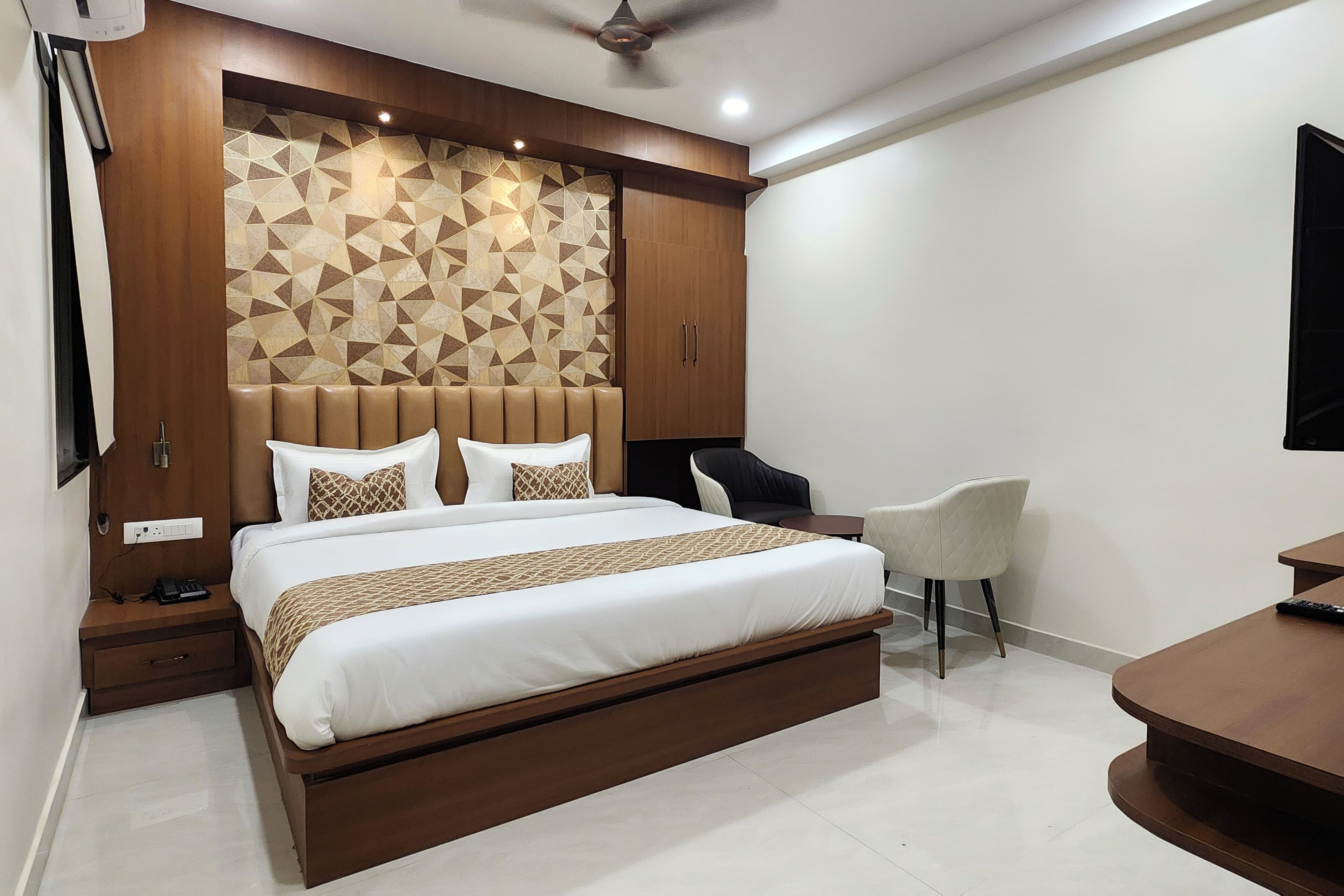 A modern bedroom with a large bed, a headboard with a geometric pattern, a bedside table, a chair, and a desk.