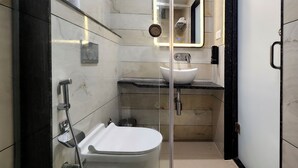 A modern bathroom with a glass-enclosed shower, a white sink, and a marble-tiled wall. - Kashi Vilaa (Varanasi)