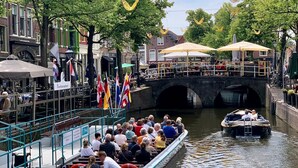 A boat with passengers on a canal, a bridge, and buildings with flags. - Cosy City Apartment Near Station, City Centre (Alkmaar)