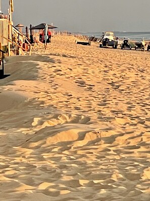A sandy beach with a wooden walkway and beach umbrellas.