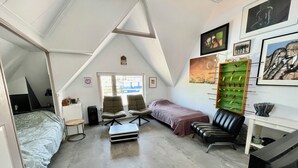 A compact room with a bed, two chairs, a desk, and a futon. There are artworks on the walls and a window providing natural light. - Cosy City Apartment Near Station, City Centre (Alkmaar)