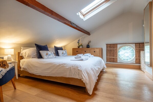 A bedroom with a large bed, wooden beams, a skylight, a wooden dresser, and a circular window.