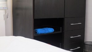 A bedroom with a bed, a dark wardrobe with multiple drawers, and a blue towel on the lower shelf. - Charming 2-Bedroom House in Ajah with AC & WiFi (ajah)