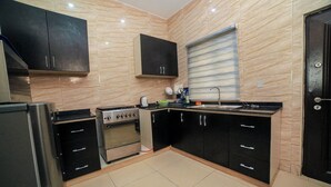 A modern kitchen with black cabinets, a stainless steel refrigerator, an oven, and a sink. - Charming 2-Bedroom House in Ajah with AC & WiFi (ajah)