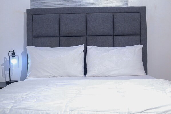 A bed with a grey upholstered headboard, white pillows, and a white bedspread.