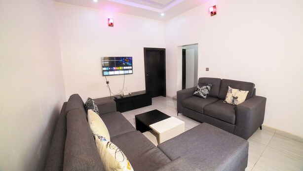 A modern living room with two grey sofas, a coffee table, and a flat-screen TV mounted on the wall. - Charming 2-Bedroom House in Ajah with AC & WiFi (ajah)