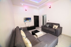 A modern living room with two grey sofas, a coffee table, and a flat-screen TV mounted on the wall.