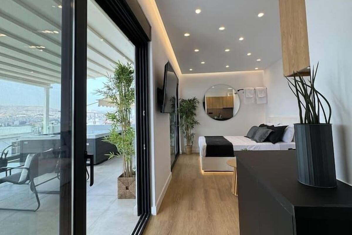A modern hotel room with a large window, a bed, a desk, and a view of the city.