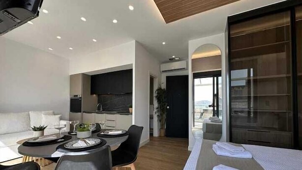 A modern hotel room with a dining area, a sofa, and a bed with towels. - BlueMotion - CentralSuite (Piraeus)