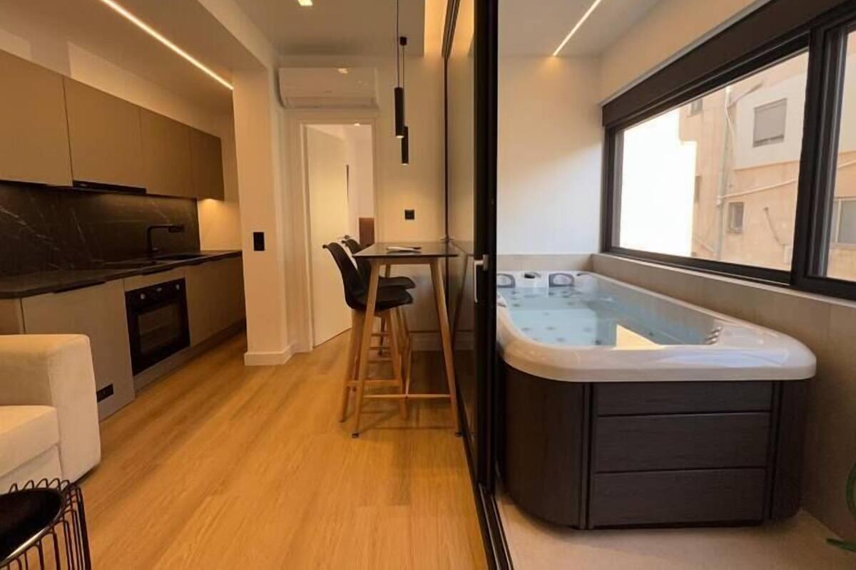 A modern kitchen with a built-in oven, a dining area with a table and chairs, and a corner bathtub with a window view.