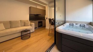 A modern living room with a sofa, a glass-enclosed hot tub, and a kitchen area. - BlueMotion - CentralSuite (Piraeus)