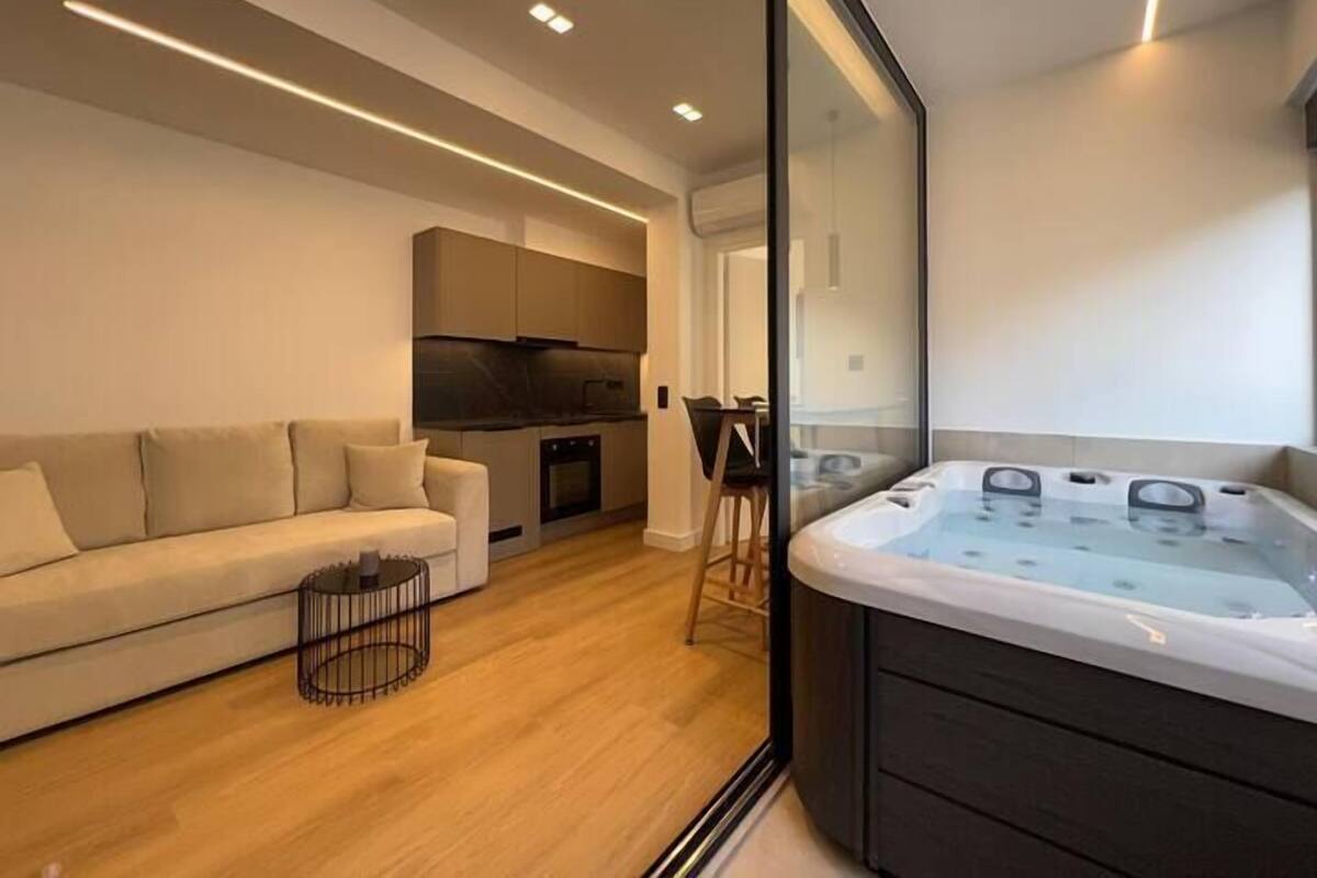 A modern living room with a sofa, a glass-enclosed hot tub, and a kitchen area.