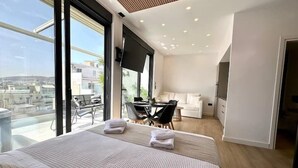A modern hotel room with a large bed, a dining area, a sofa, and a TV. - BlueMotion - CentralSuite (Piraeus)