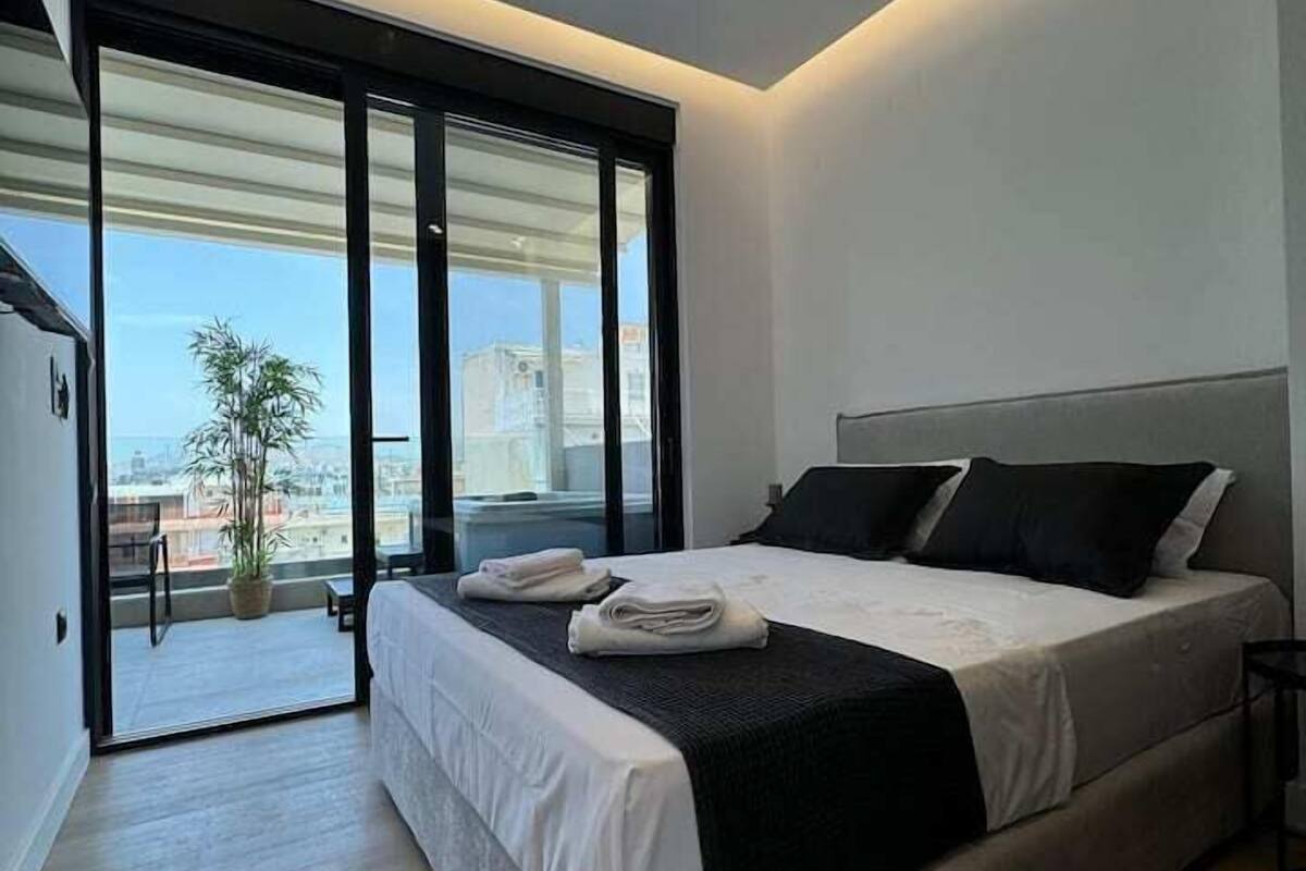 A modern bedroom with a large bed, a sliding glass door leading to a balcony, and a city view.
