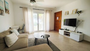 Un salon comprenant un canapé, une table basse, un téléviseur et une porte-fenêtre coulissante donnant sur un balcon.