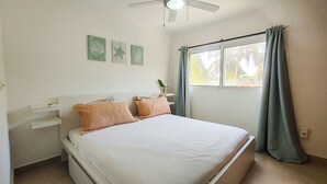 Une chambre à coucher avec un lit, un ventilateur de plafond, une fenêtre avec des rideaux et des œuvres d’art murales.
