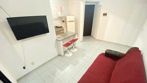 A compact living space with a red sofa, a small kitchenette, and a flat-screen TV mounted on the wall.