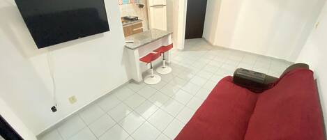 A compact living space with a red sofa, a small kitchenette, and a flat-screen TV mounted on the wall.