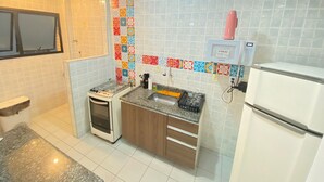 A compact kitchen with white tiled walls, a small oven, a sink with a cutting board, and a white refrigerator.
