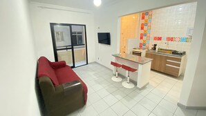 A compact living space with a kitchenette, a red sofa, a ceiling fan, and a sliding glass door leading to an outdoor area.