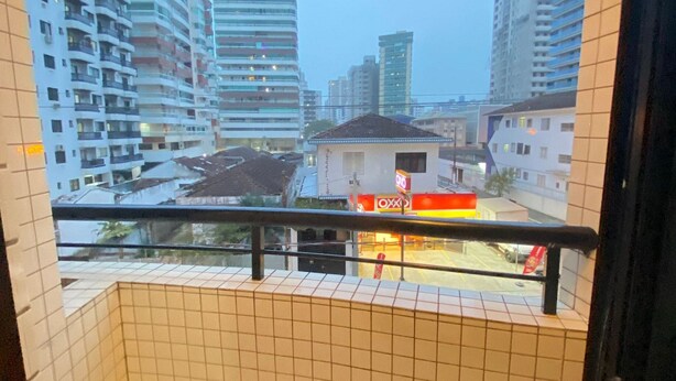 A view from a balcony with tiled walls and floor, overlooking a cityscape with high-rise buildings and a small shop with a red and white sign.