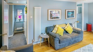 A living room with a sofa, a small round table, a radiator, and two framed pictures on the wall. - Queens Quarter 2-Bed | Next to City Centre - Pass the Keys (Belfast)
