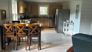 A modern kitchen with wooden cabinets, a stainless steel refrigerator, and a dining area with wooden chairs.