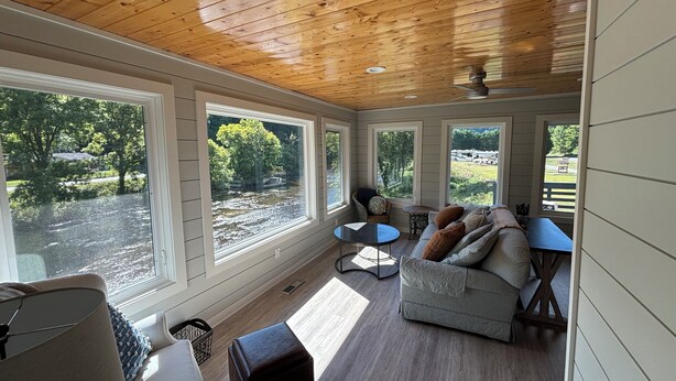 A cozy room with a wooden ceiling, large windows, a sofa, a small table, and a lamp.