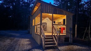 Une cabane en bois dotée d’une grande fenêtre, d’un escalier menant à l’entrée et d’une tente à l’intérieur.