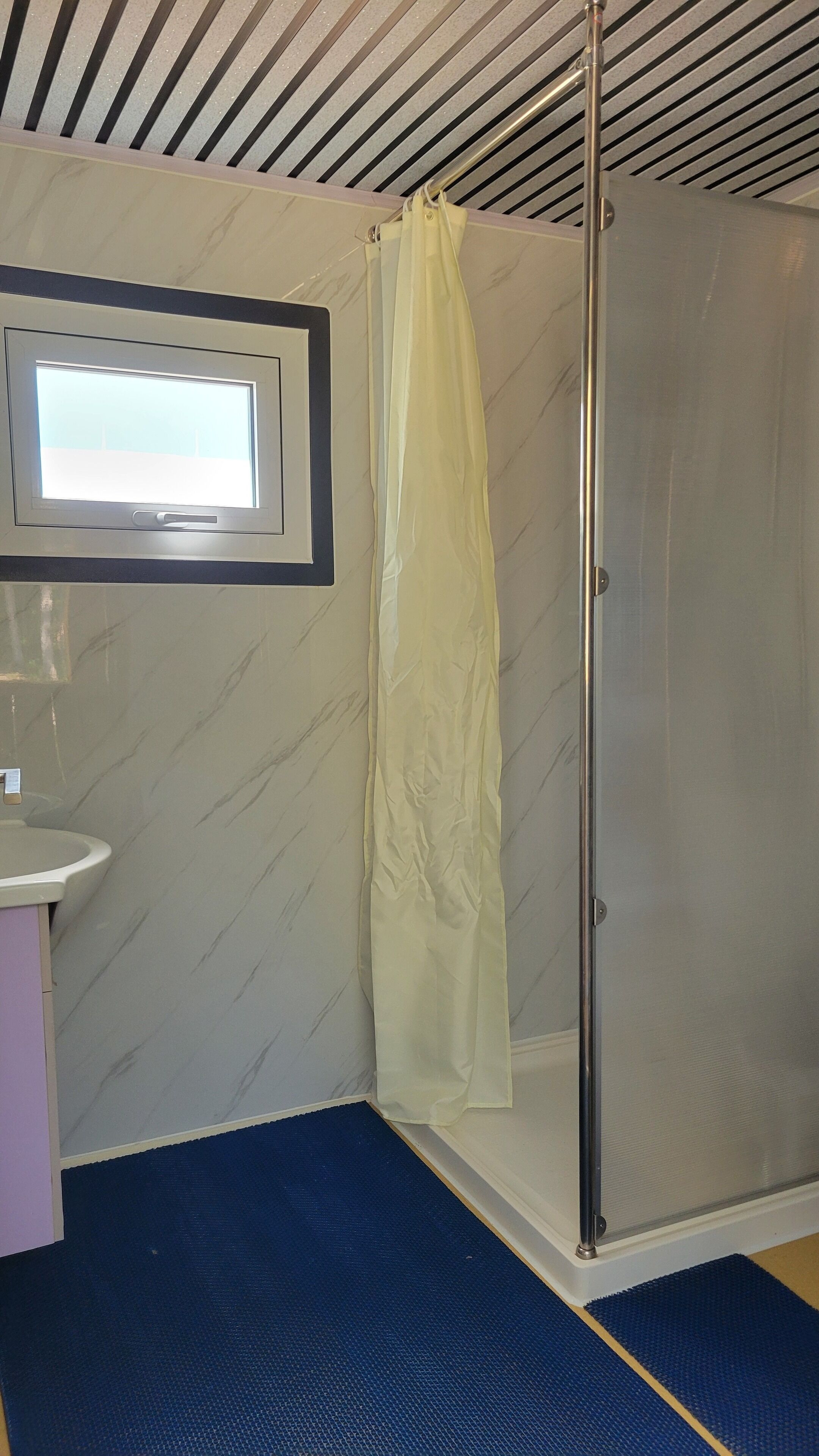 A bathroom with a shower, a sink, and a window.