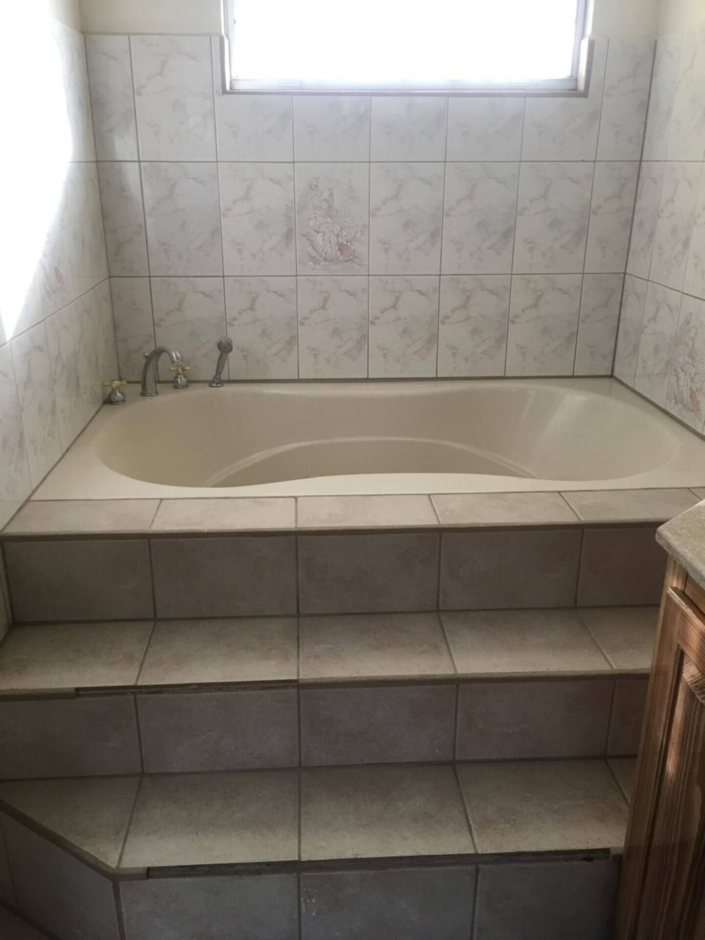 Ein Badezimmer mit Badewanne, gefliesten Wänden und einem Fenster.