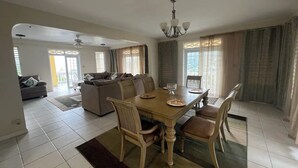 Un'ampia zona giorno con tavolo da pranzo, sedie e divano. Sopra il tavolo c'è un lampadario e nella zona giorno una ventola a soffitto.
