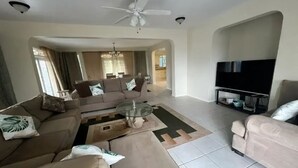 Un ampio soggiorno con ventilatore a soffitto, televisione a schermo piatto e zona pranzo con tavolo e sedie in vetro.