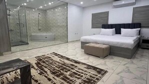 A modern bedroom with a large bed, a bench, a glass shower enclosure, and a marble floor. - Habu Pyramids View Hotel (Giza)