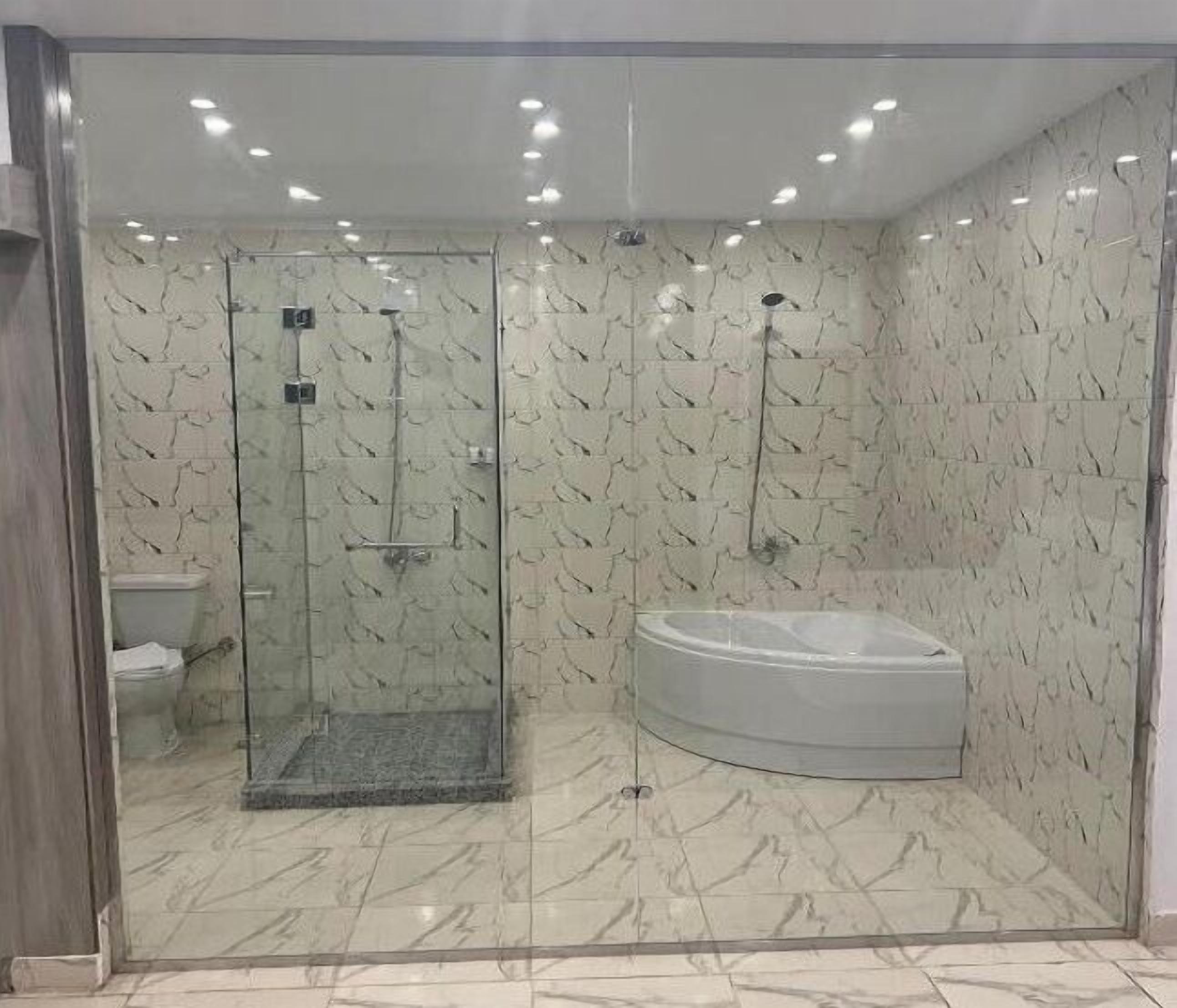 A modern bathroom with a glass-enclosed shower, a white bathtub, and marble-patterned walls.