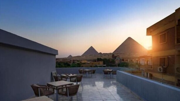 A rooftop terrace with tables and chairs, offering a view of the pyramids at sunset. - Habu Pyramids View Hotel (Giza)