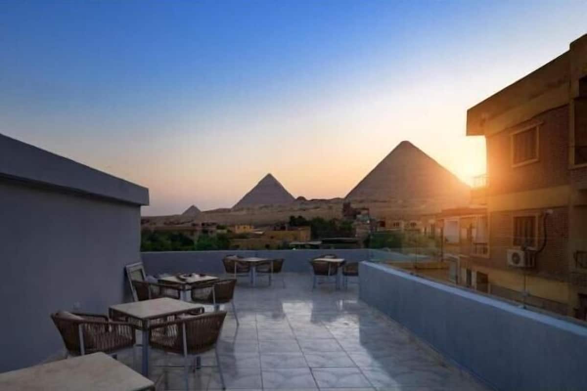 A rooftop terrace with tables and chairs, offering a view of the pyramids at sunset.