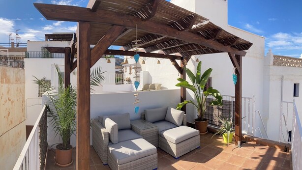 A covered outdoor seating area with wicker furniture and potted plants.