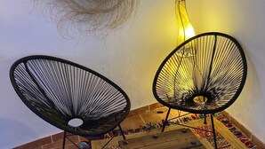 Two black wireframe chairs with wooden side tables, a woven wall hanging, and a wall-mounted mirror.